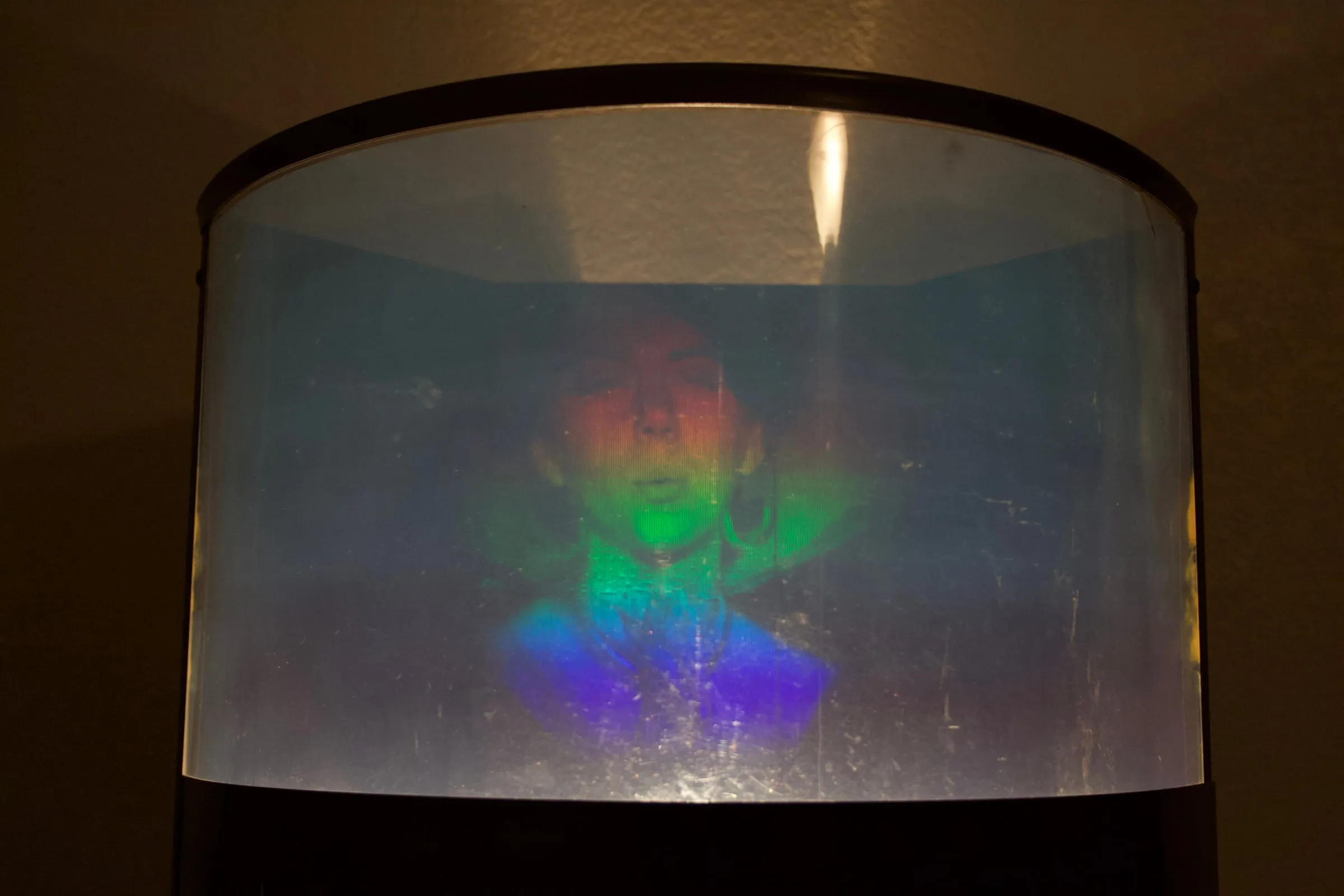 A rainbow multiplex hologram portrait of a person, displayed in a cylindrical hologram display.